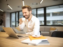 depth of field photo of man sitting on chair while holding cup in front of table