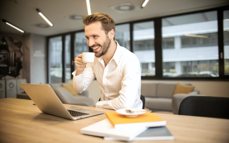 depth of field photo of man sitting on chair while holding cup in front of table