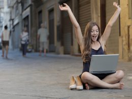 Woman Raising Her Hands Up While Sitting on Floor With Macbook Pro on Lap
