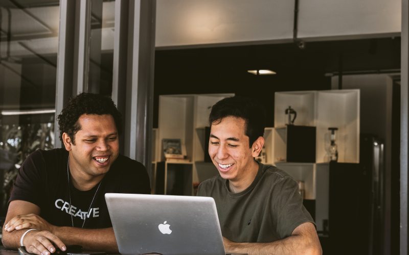 two smiling men looking at MacBook