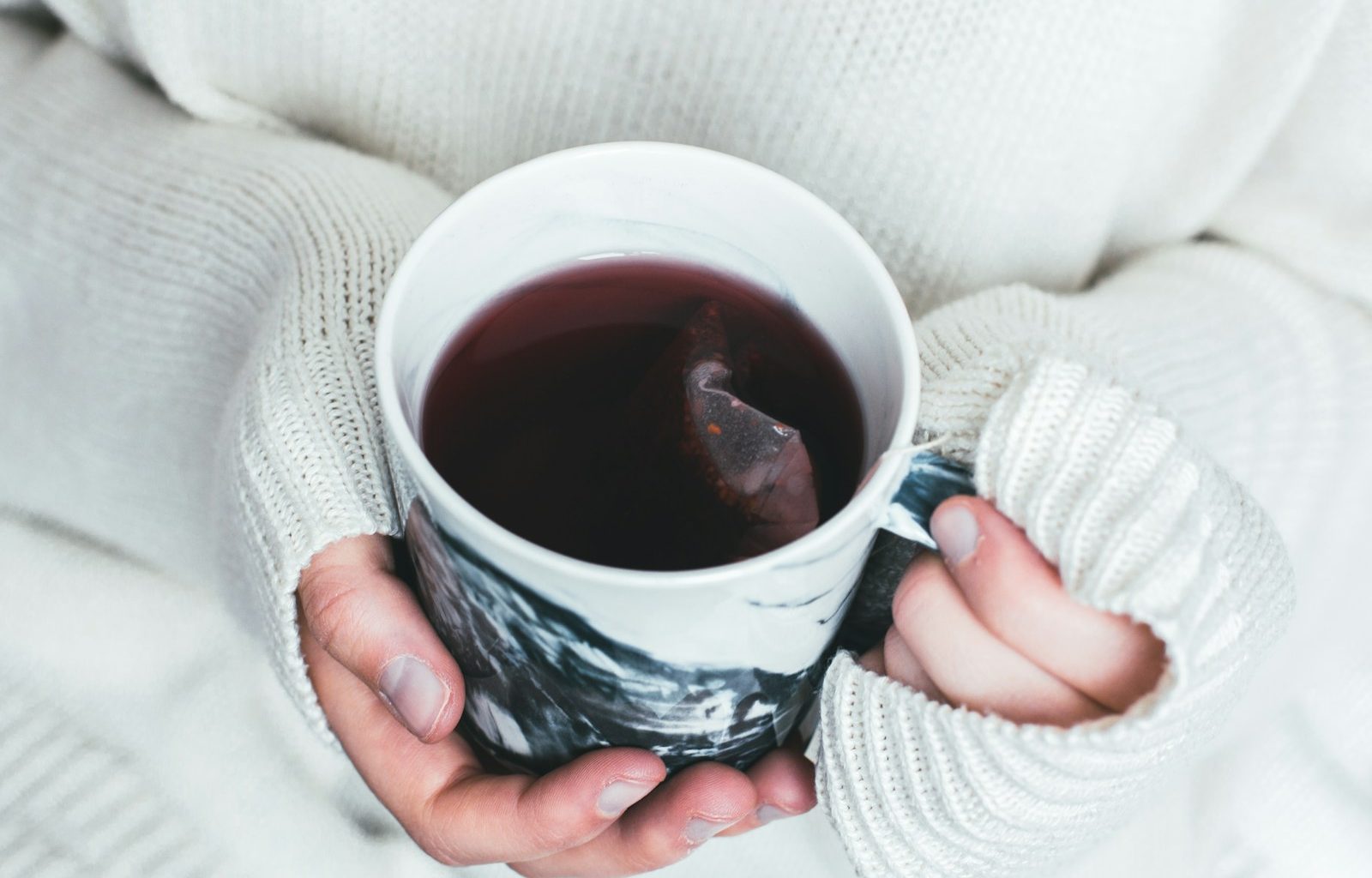 person holding white and black cup with teabag inside