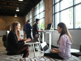 two women sitting on a bed using laptops