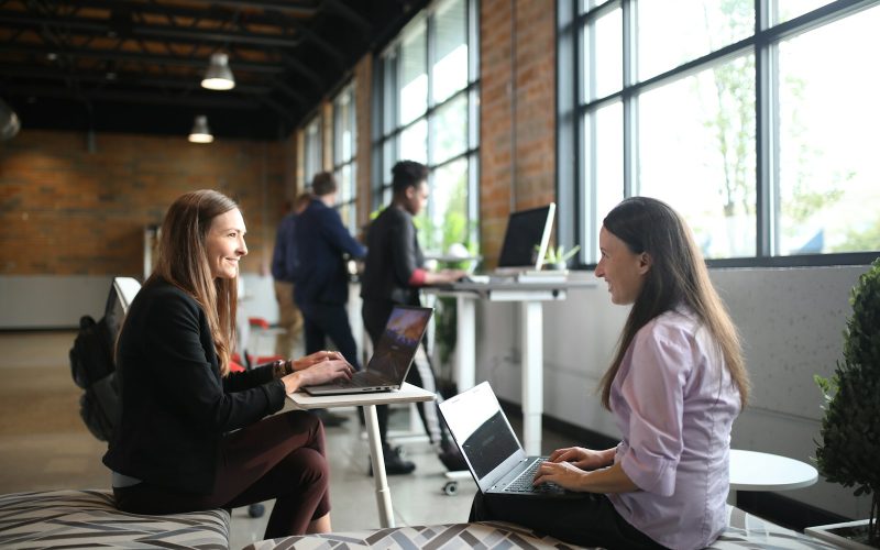 two women sitting on a bed using laptops