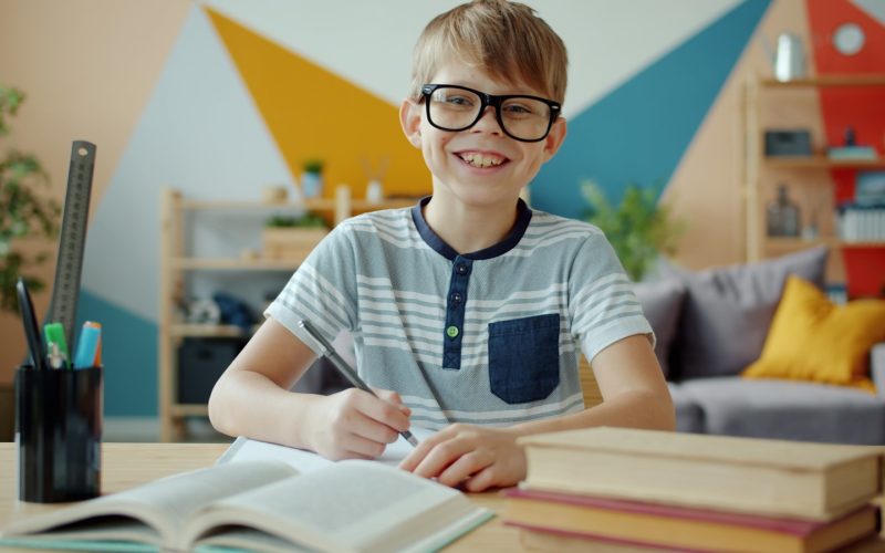 Smiling boy wearing glasses studying at a desk.